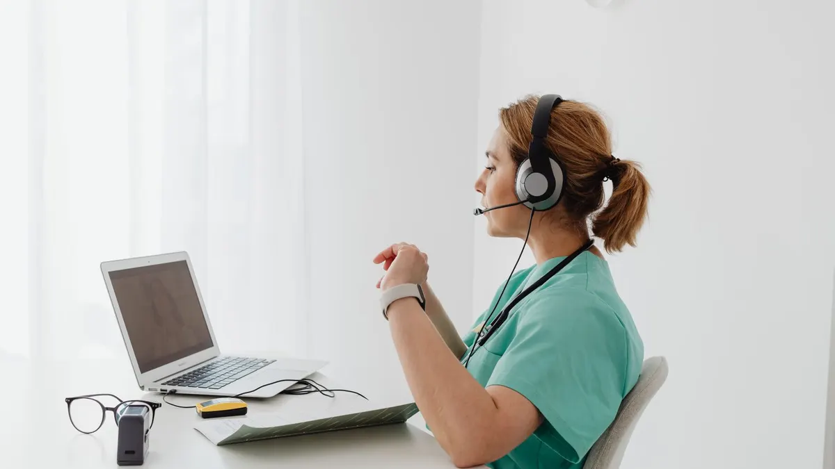 Profesional sanitaria con auriculares y micrófono atendiendo una videoconsulta frente a su portátil